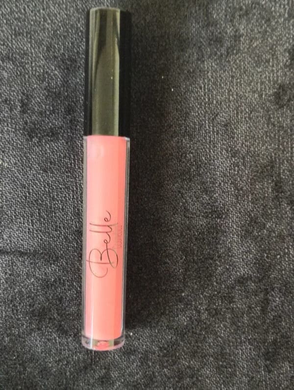 A pink lip gloss sitting on top of a gray surface.